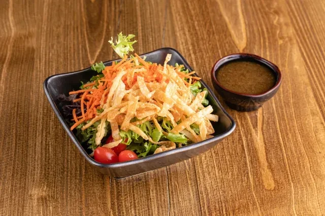 Salad with carrots, crispy strips, tomatoes, dressing on wooden table.