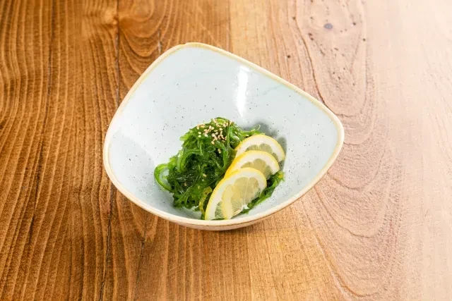 Green seaweed salad garnished with lemon and sesame in a blue bowl.