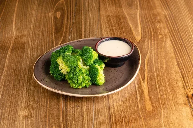 Vibrant green broccoli florets with creamy white dipping sauce on a plate.