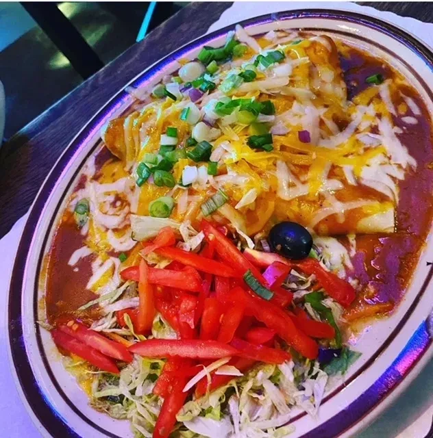 Plate of enchiladas with melted cheese, red sauce, onions, lettuce, tomato.