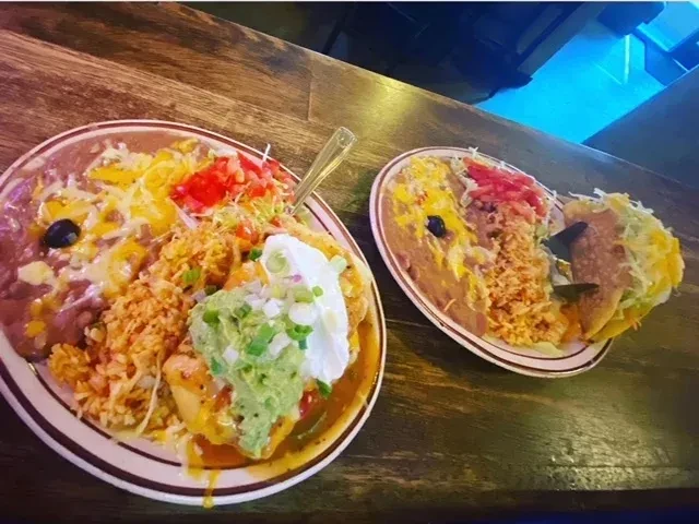 Two plates of Mexican food on a dark rustic table.