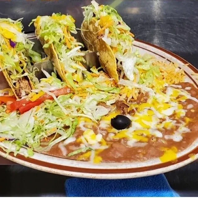 Plate of three hard-shell tacos, refried beans, and Spanish rice.