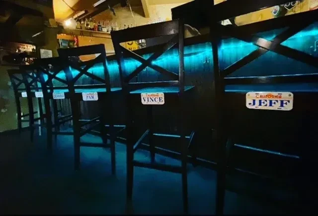Empty bar stools under a turquoise LED-lit bar with name tags.
