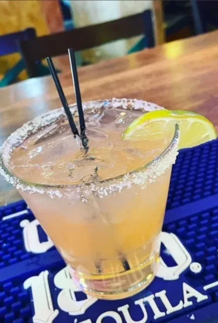 Peachy-orange cocktail with lime, salted rim, on blue bar mat.
