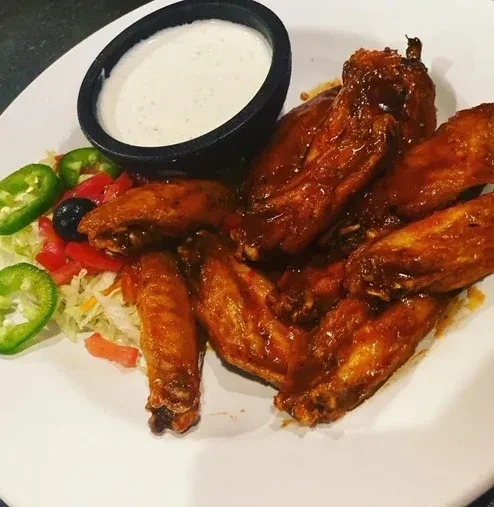 Plate of dark-sauced chicken wings with dip and vegetable garnish.