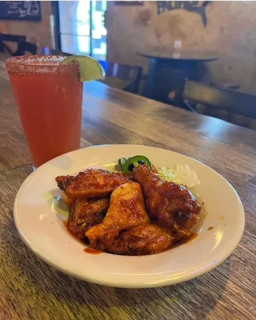 Glossy chicken wings, jalapeños, and a pink chili-rimmed drink.