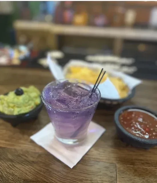 Close-up of purple drink, guacamole, salsa, and chips on a wooden table.