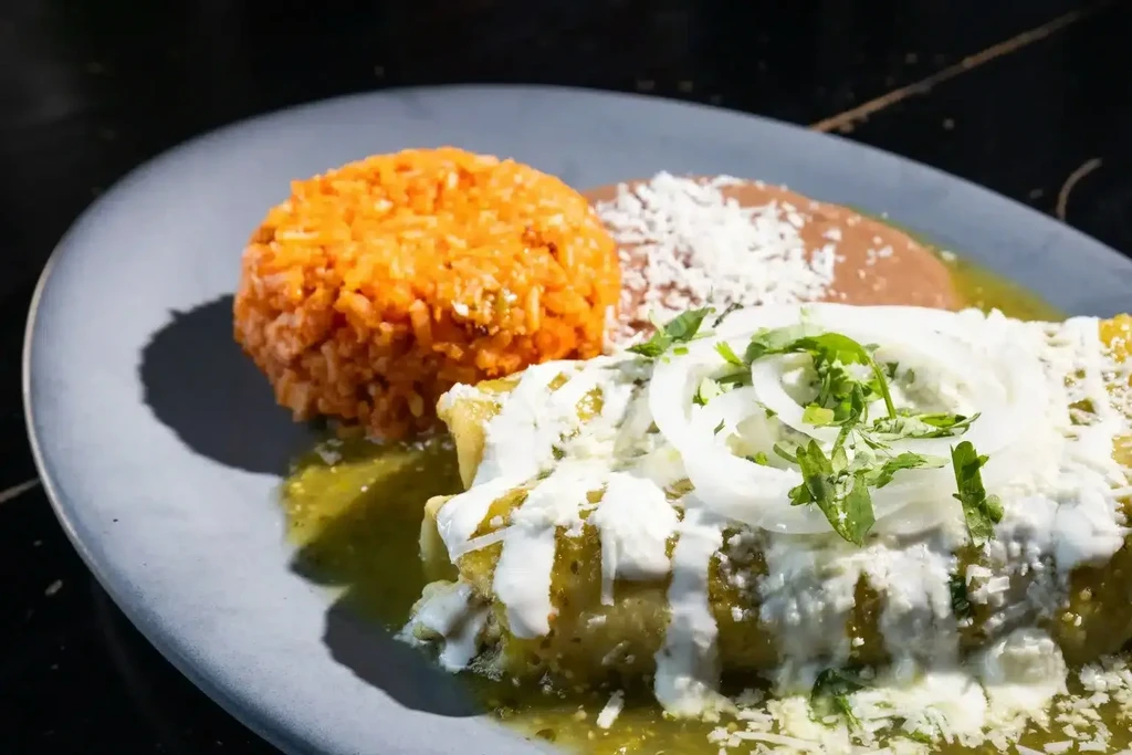 Close-up of Mexican rice, refried beans, and green enchiladas.
