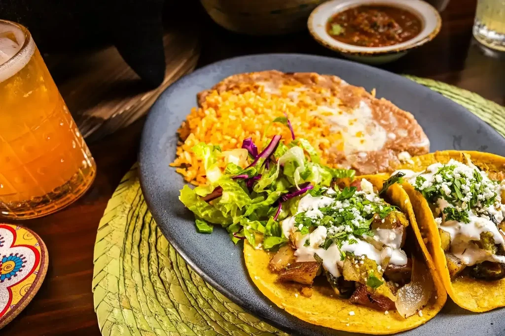 Colorful Mexican plate with two tacos, rice, beans, and salad.