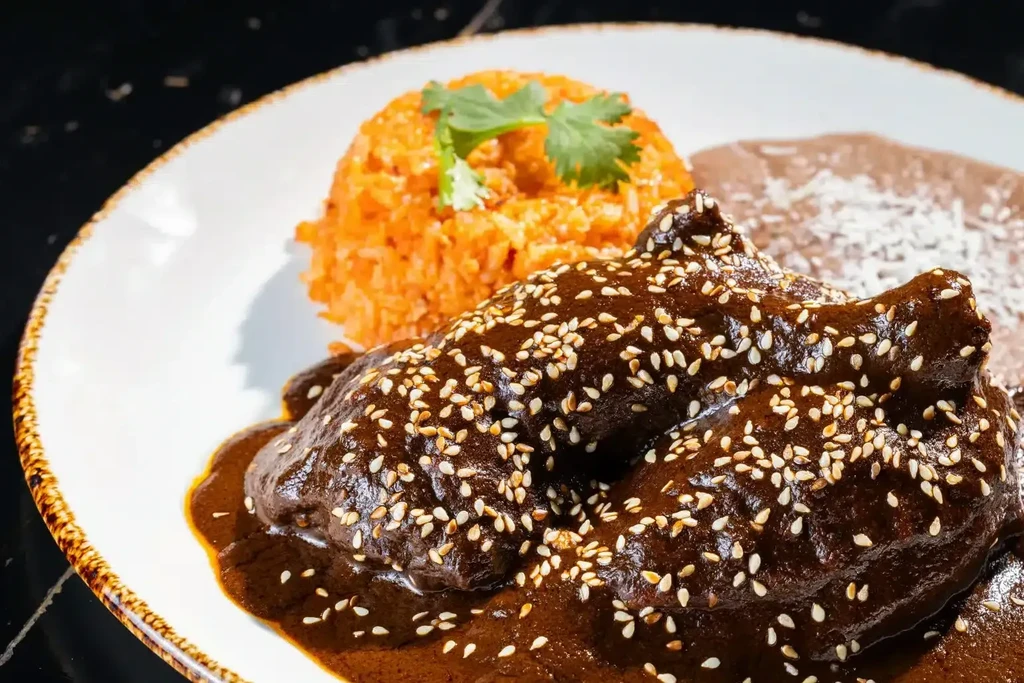 Chicken mole, Mexican rice, and refried beans on a white plate.