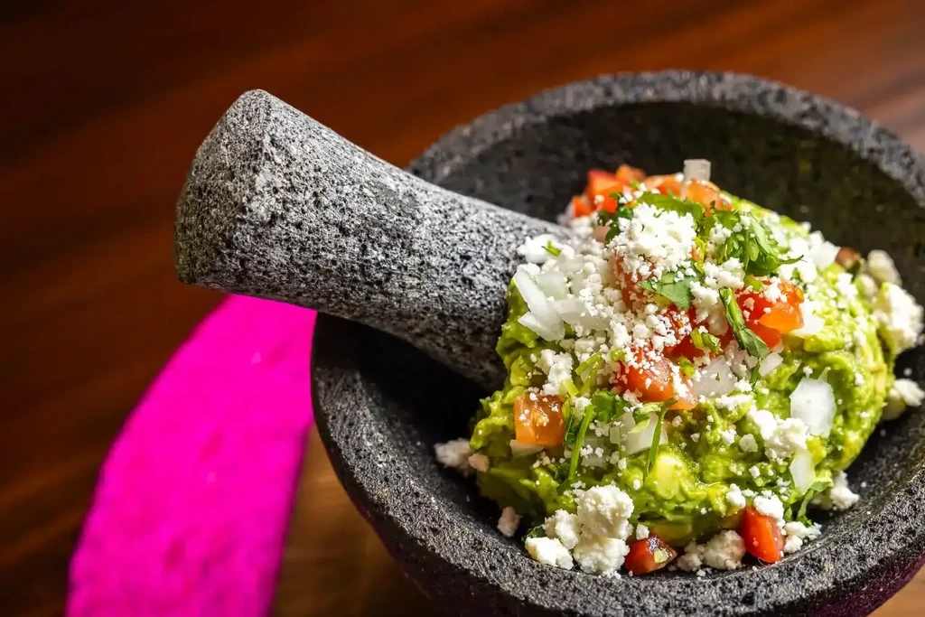 Vibrant guacamole in molcajete with tomatoes, onions, cheese, cilantro.