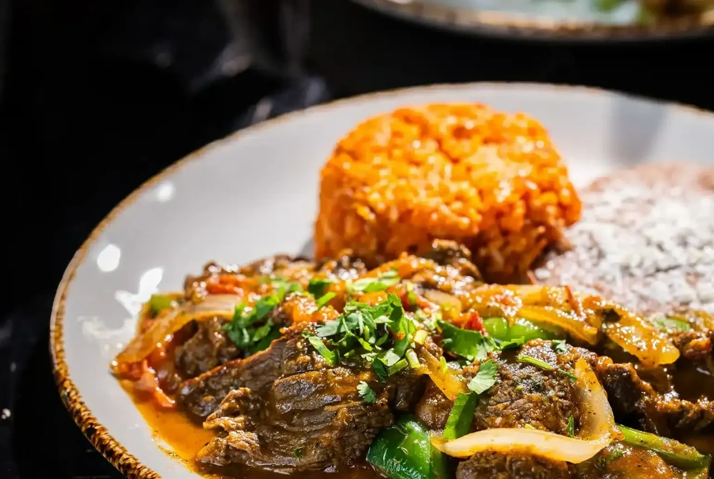 Braised beef strips, sautéed vegetables, Spanish rice, and refried beans.