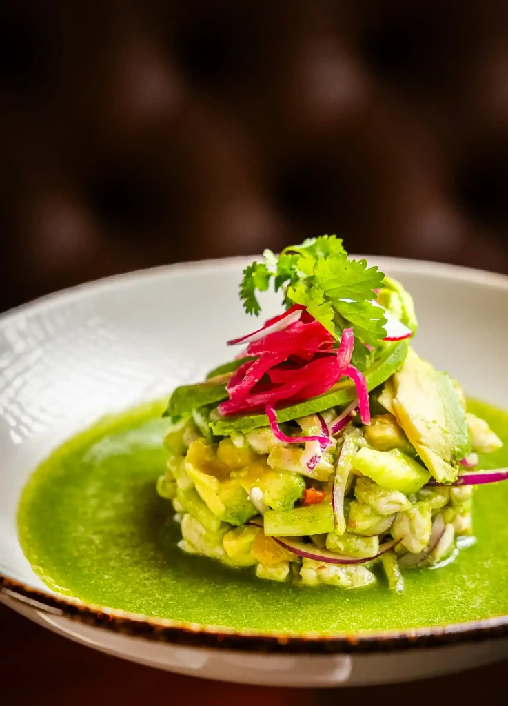 Vibrant avocado and seafood ceviche tower with green sauce and garnishes.