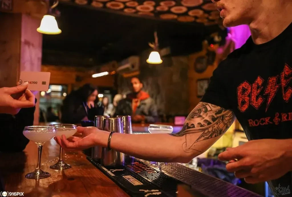 Bartender serves two cocktails as customer presents a discount card.