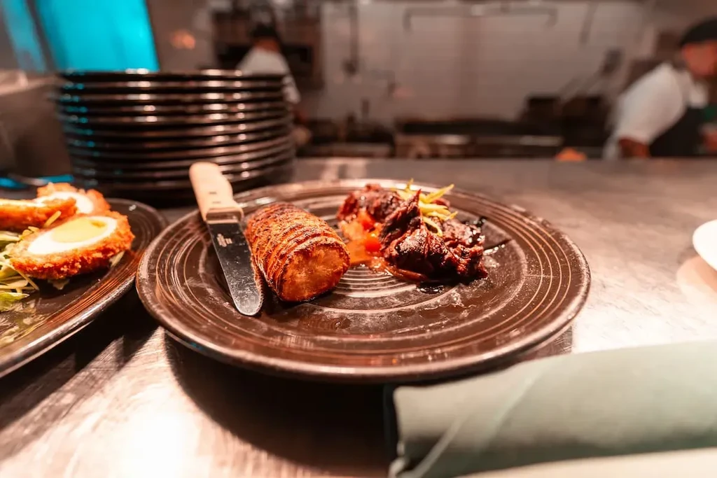 Two plates of food, Scotch eggs and meat, on a kitchen counter.