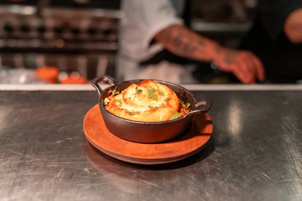 Savory golden pie in cast-iron skillet, chef's tattooed arm.