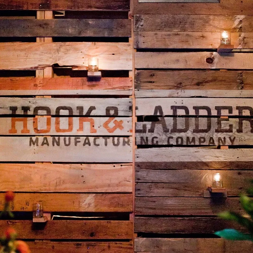 Rustic wooden pallet wall with "HOOK & LADDER" text and lit candles.