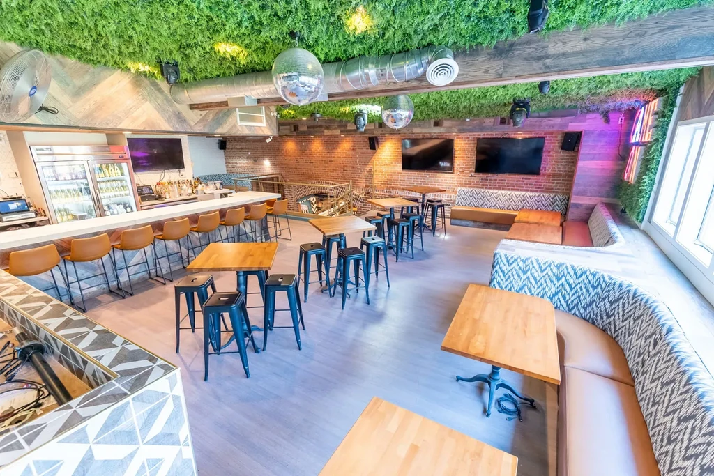 Restaurant interior with green foliage ceiling, disco balls, bar, and seating.