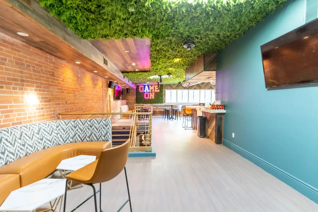 Vibrant modern restaurant with a 'GAME ON' neon sign and green foliage ceiling.