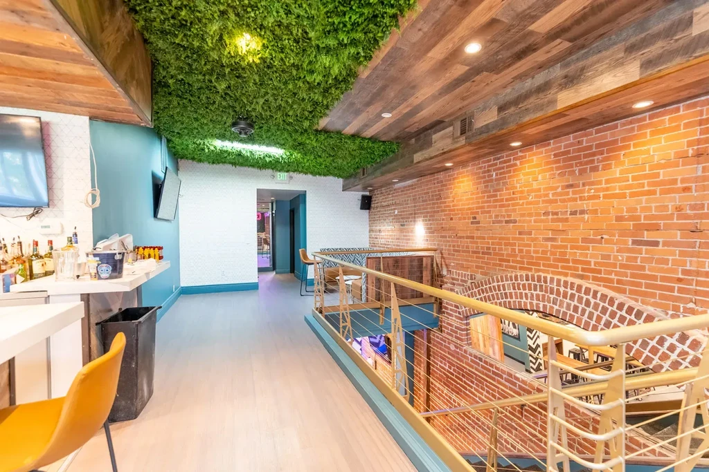 Vibrant restaurant interior with a bar, green moss ceiling, and exposed brick.