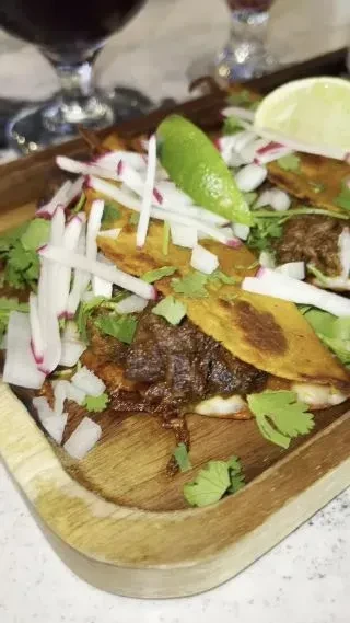 Tacos with meat, radish, cilantro, and lime on a wooden board.