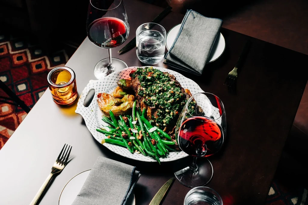 Elegantly plated roasted meal, wine, and water on a dark table.