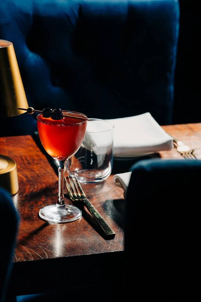 Close-up of reddish-orange cocktail with cherries on a dark wooden table.
