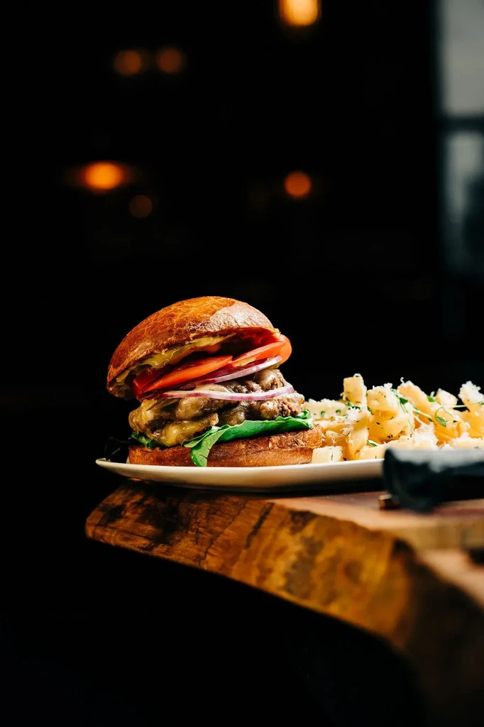 Double-patty gourmet burger, cheesy fries, dark restaurant background.
