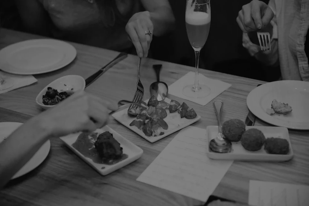Black and white photo of hands sharing small plates of food.