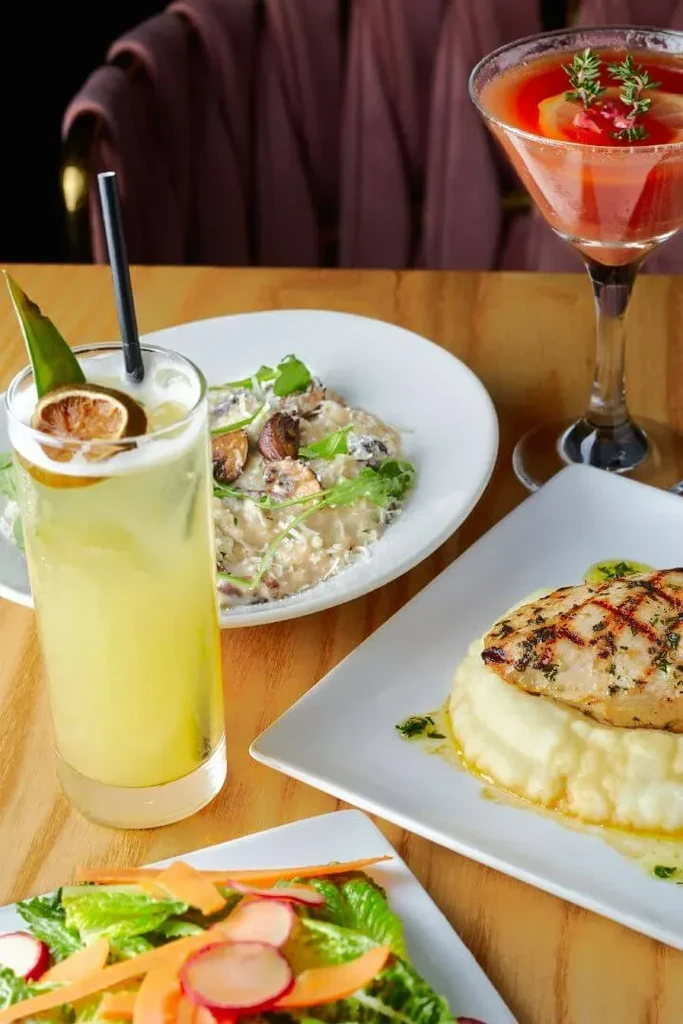 Grilled chicken, risotto, salad, and cocktails on a wooden table.