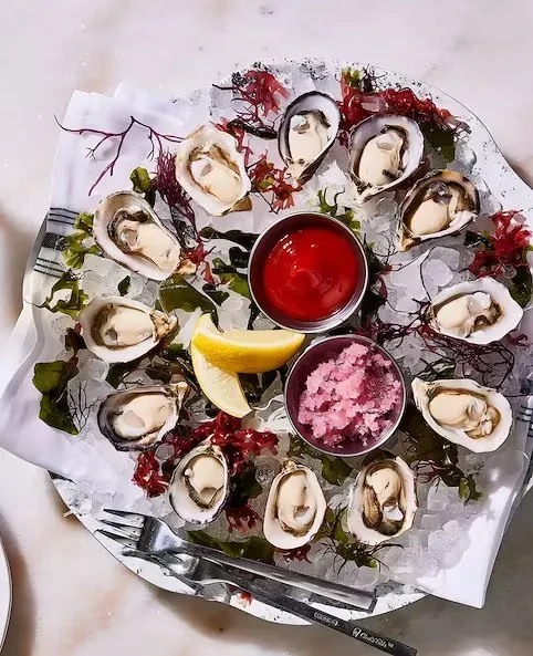 Platter of twelve fresh shucked oysters on ice with lemon and sauce.