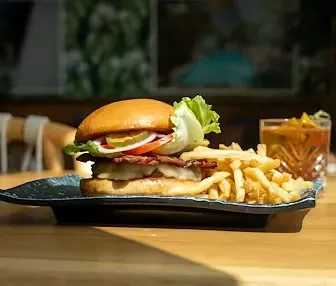 Gourmet burger, crinkle-cut fries, and amber drink on a dark plate.