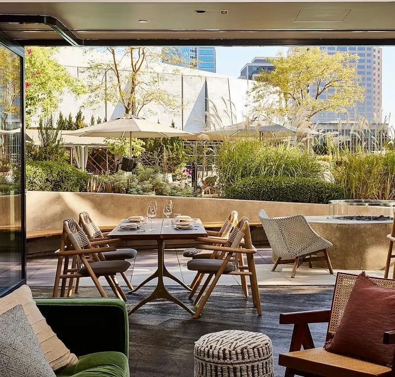 Elegant outdoor dining terrace with set table, lush plants, and city view.