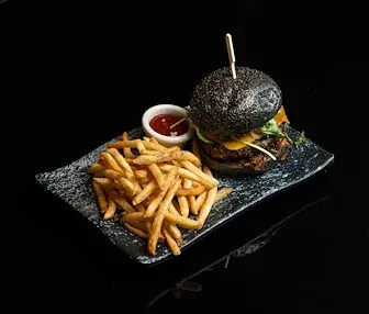 Black bun burger, golden fries, red sauce on dark plate.