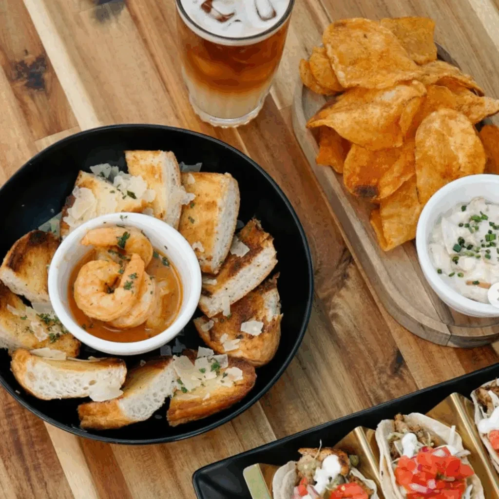 Overhead photo of shrimp, bread, chips, tacos, and a layered iced drink.