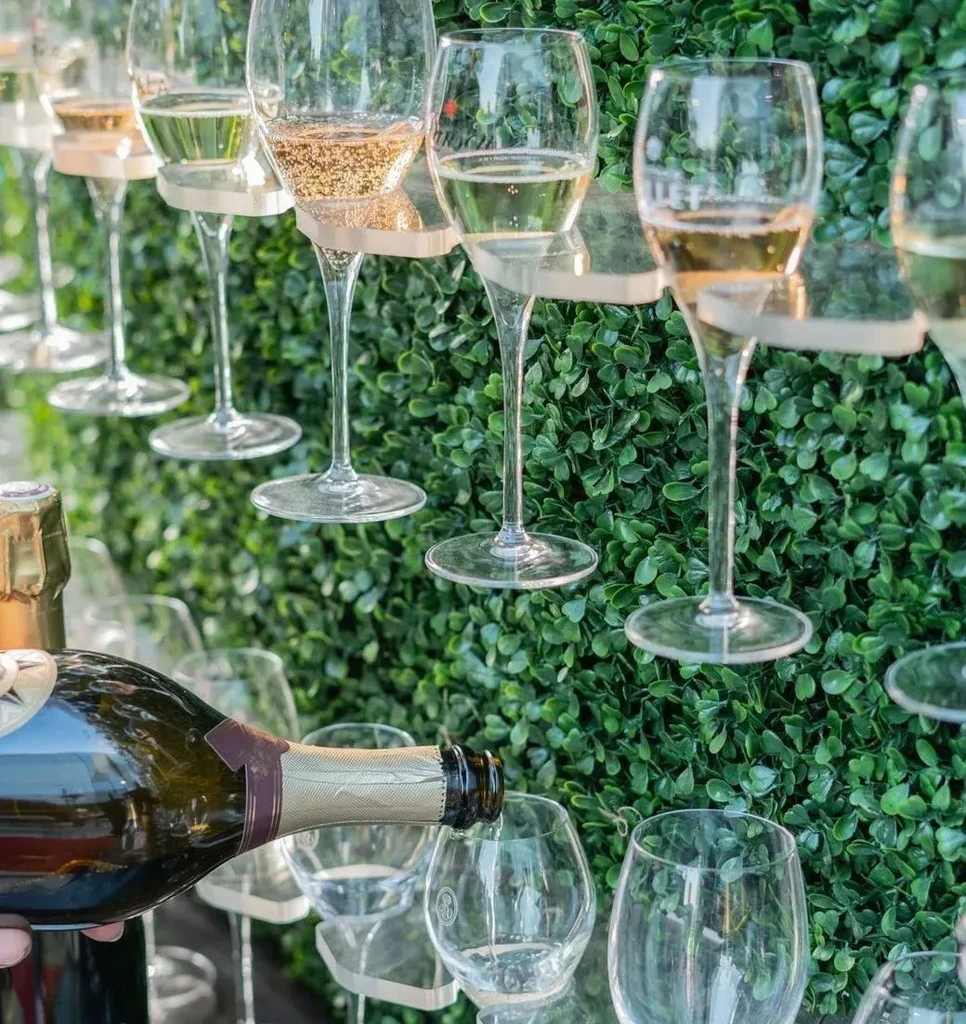 Hand pours sparkling wine into glasses on a green wall display.