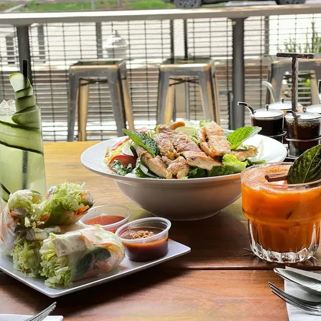 Vibrant meal with spring rolls, meat salad, and drinks on a wooden table.