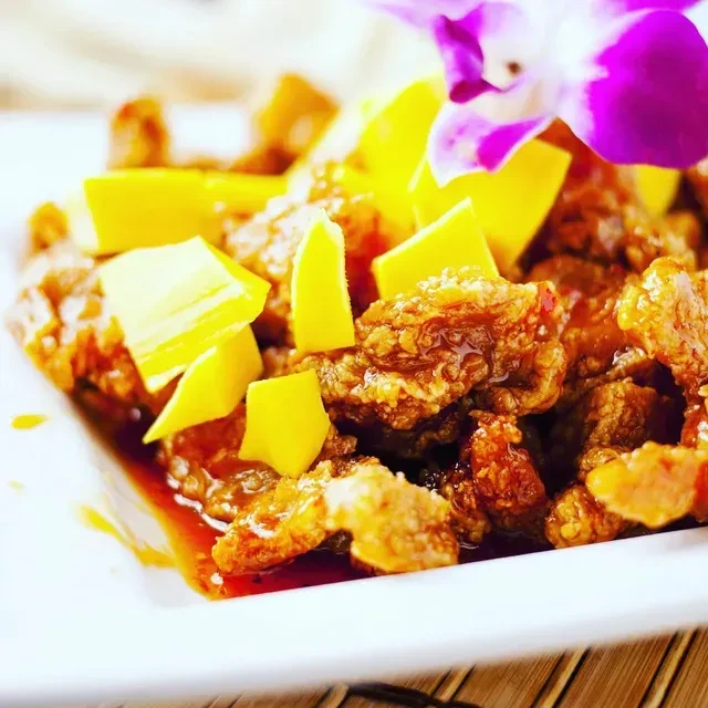 Crispy meat with yellow fruit, reddish-brown sauce, and orchid garnish.