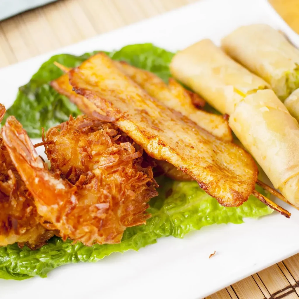 Appetizer platter with crispy coconut shrimp, grilled meat skewers, and spring rolls.