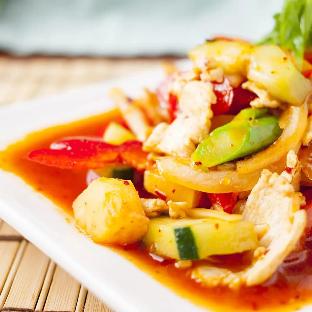 Chicken, pineapple, bell pepper, onion stir-fry with reddish-orange sauce.
