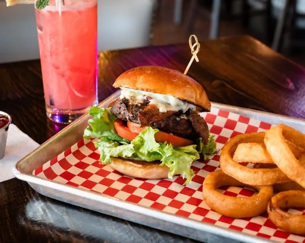 Close-up of a burger with bacon and onion rings on a tray.
