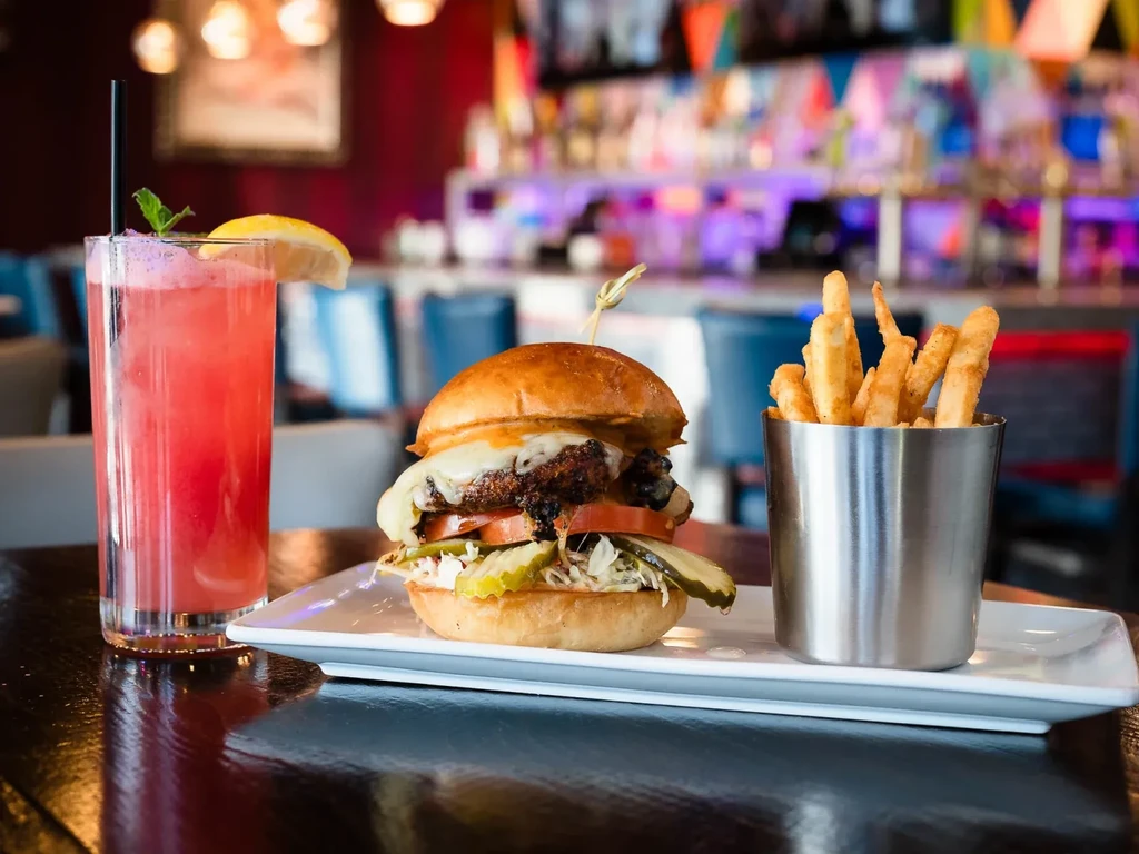 Gourmet burger, golden fries, and pink drink on a reflective table.
