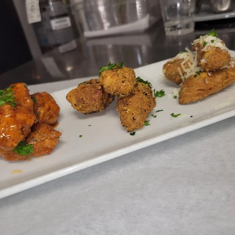 White plate with three chicken appetizers, herbs, and cheese.