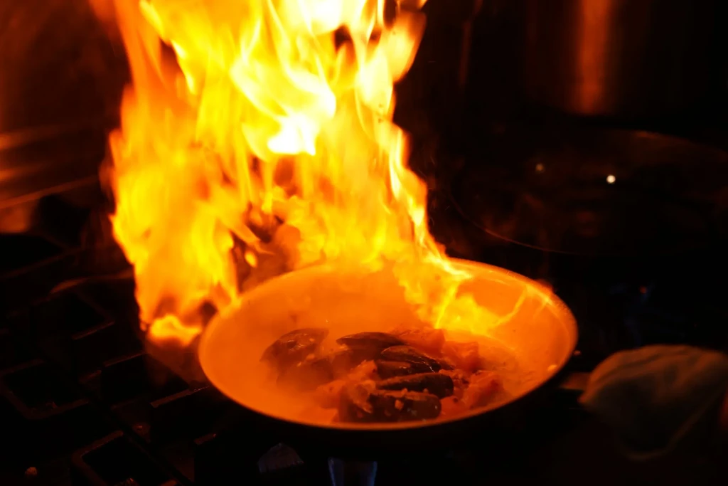 Seafood flambéing in a pan on a stove with vibrant orange flames.
