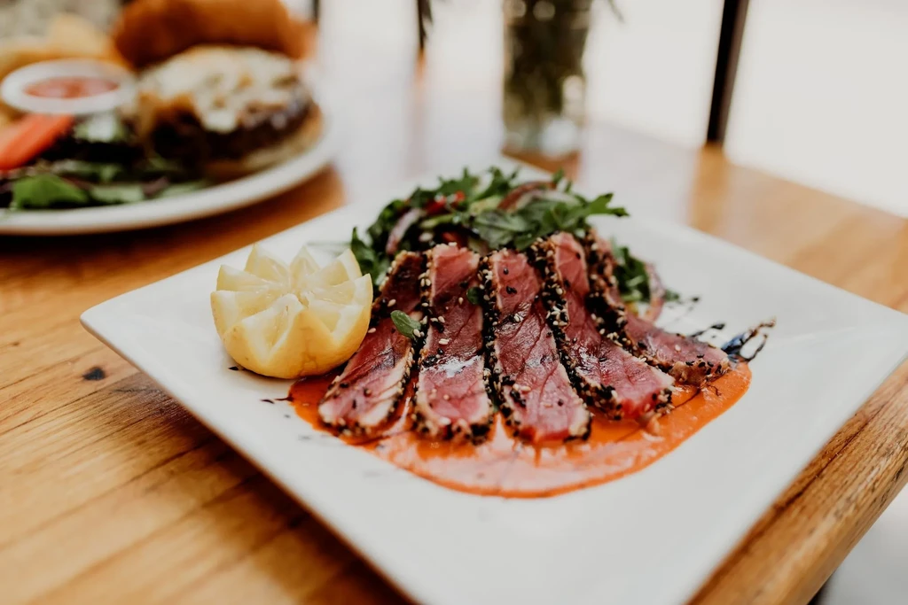 Rare seared sesame tuna, sliced, with sauce, greens, and lemon.