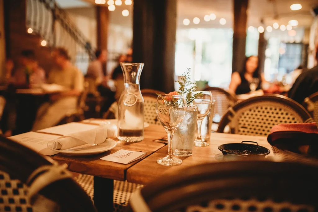 Restaurant table set with water, glasses, bread, blurred patrons.