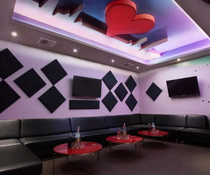 Modern, empty karaoke room with sofa, TVs, and purple party lighting.