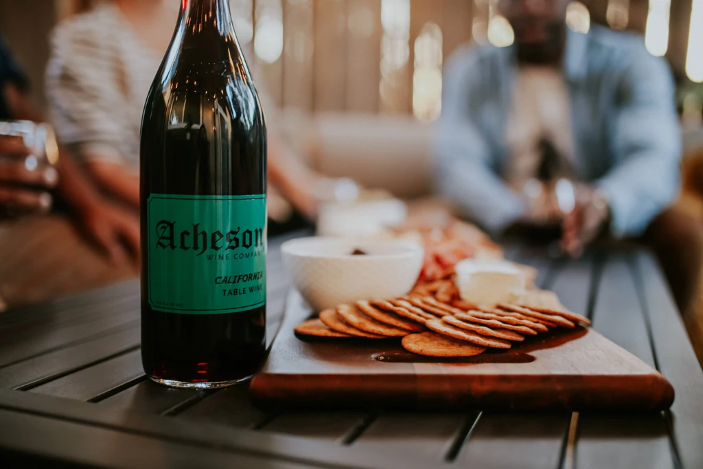 Acheson wine bottle, crackers, dip, and cheese on a table.