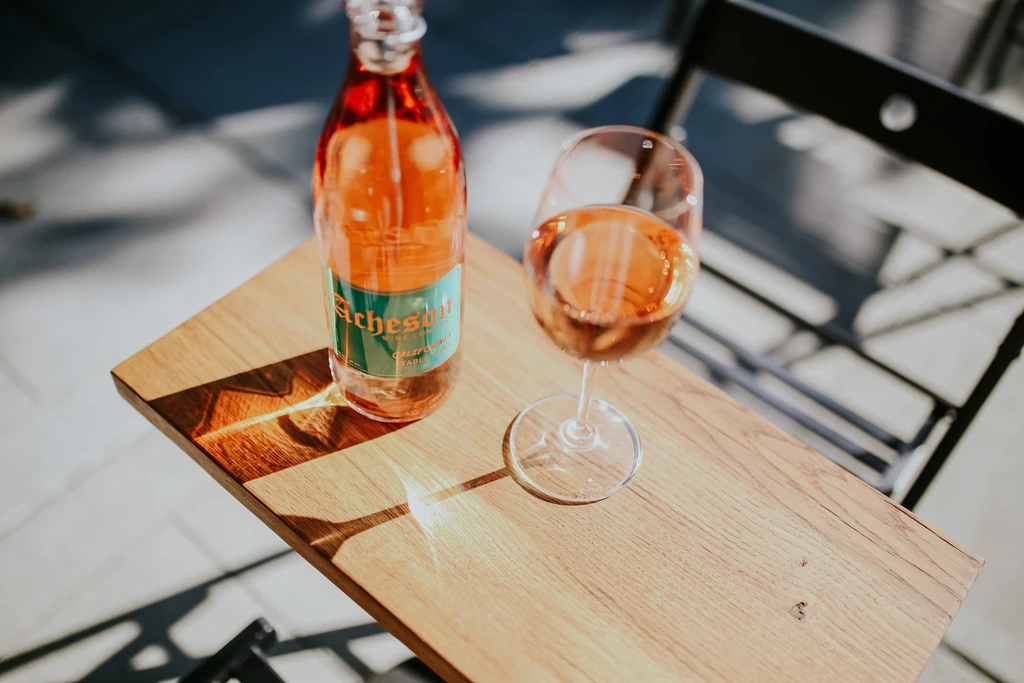 Acheson rosé wine bottle and glass on a sunlit wooden table.