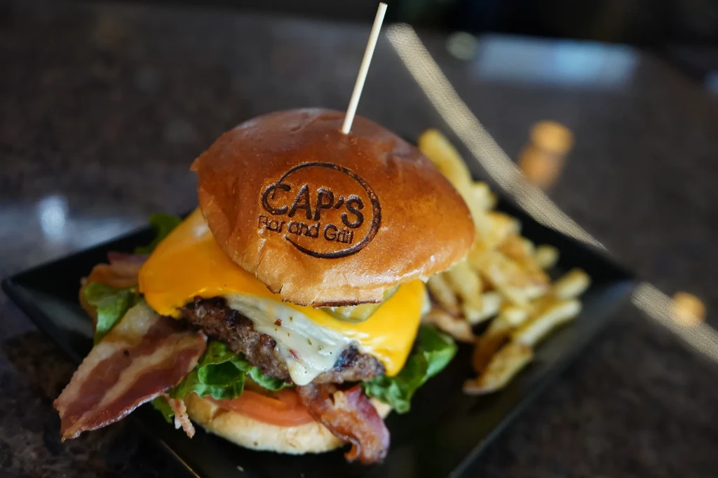 CAP'S Bar and Grill burger with bacon, cheese, and french fries.